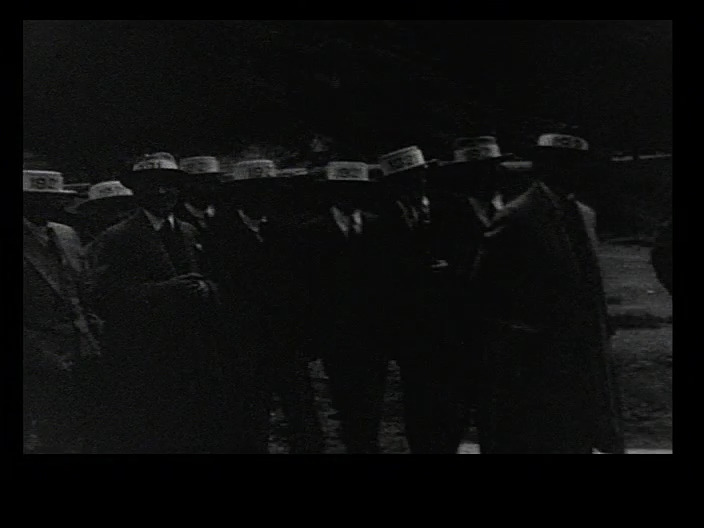 Black and white image of men in suits and straw hats
